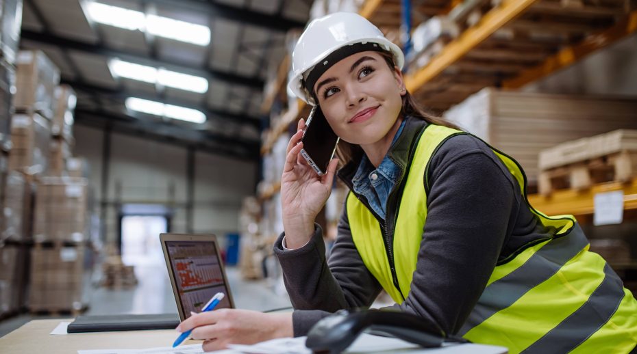 Woman wearing a hardhat on phone in warehouse